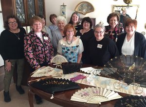 Eleven attendees of the first Midwest Regional Conference in Springfield, Illinois pose for a group photo behind a table covered with antique fans.